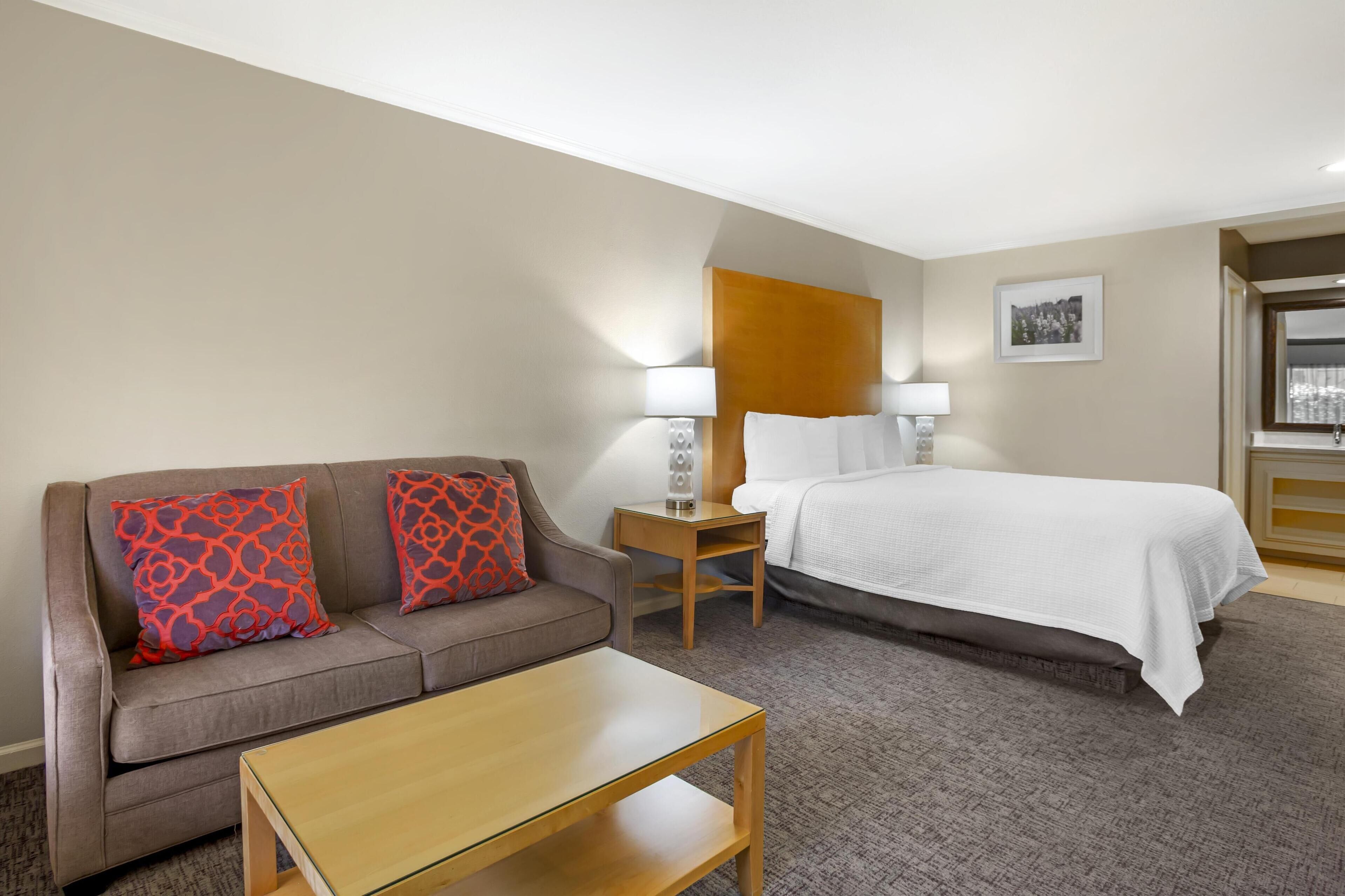 Een hotelkamer met een bank, een bed, een nachtkastje en een lamp.