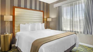 Een hotelkamer met een groot bed, twee bedlampen, een raam met dunne gordijnen en een kamerbreed tapijt met een patroon.