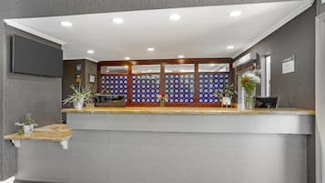 A reception area with a counter, a wall-mounted TV, and a decorative blue and white patterned partition.