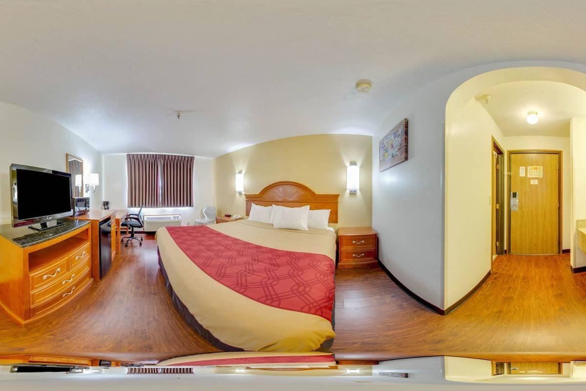A hotel room with a bed, desk, TV, and a bathroom visible through an archway.
