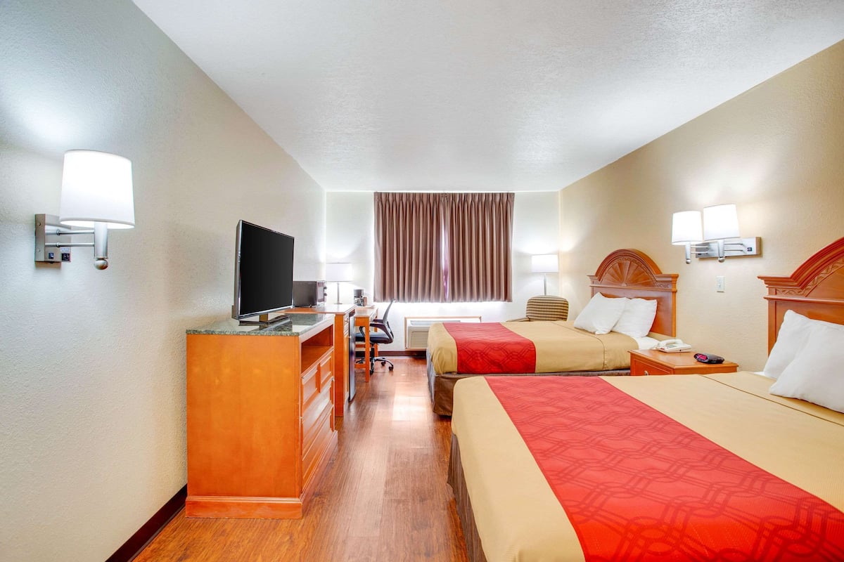 A hotel room with two beds, a desk, a television, and a window with curtains.