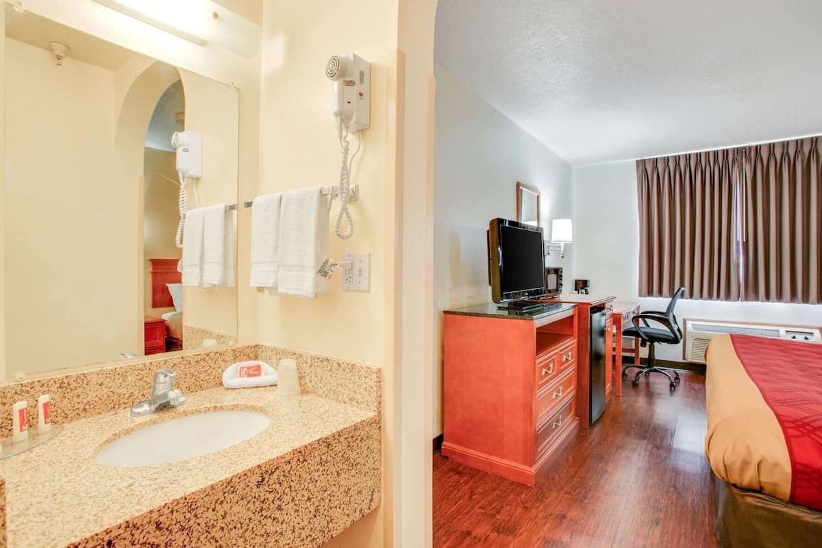 A hotel room with a bathroom, a TV, a desk, and a bed.