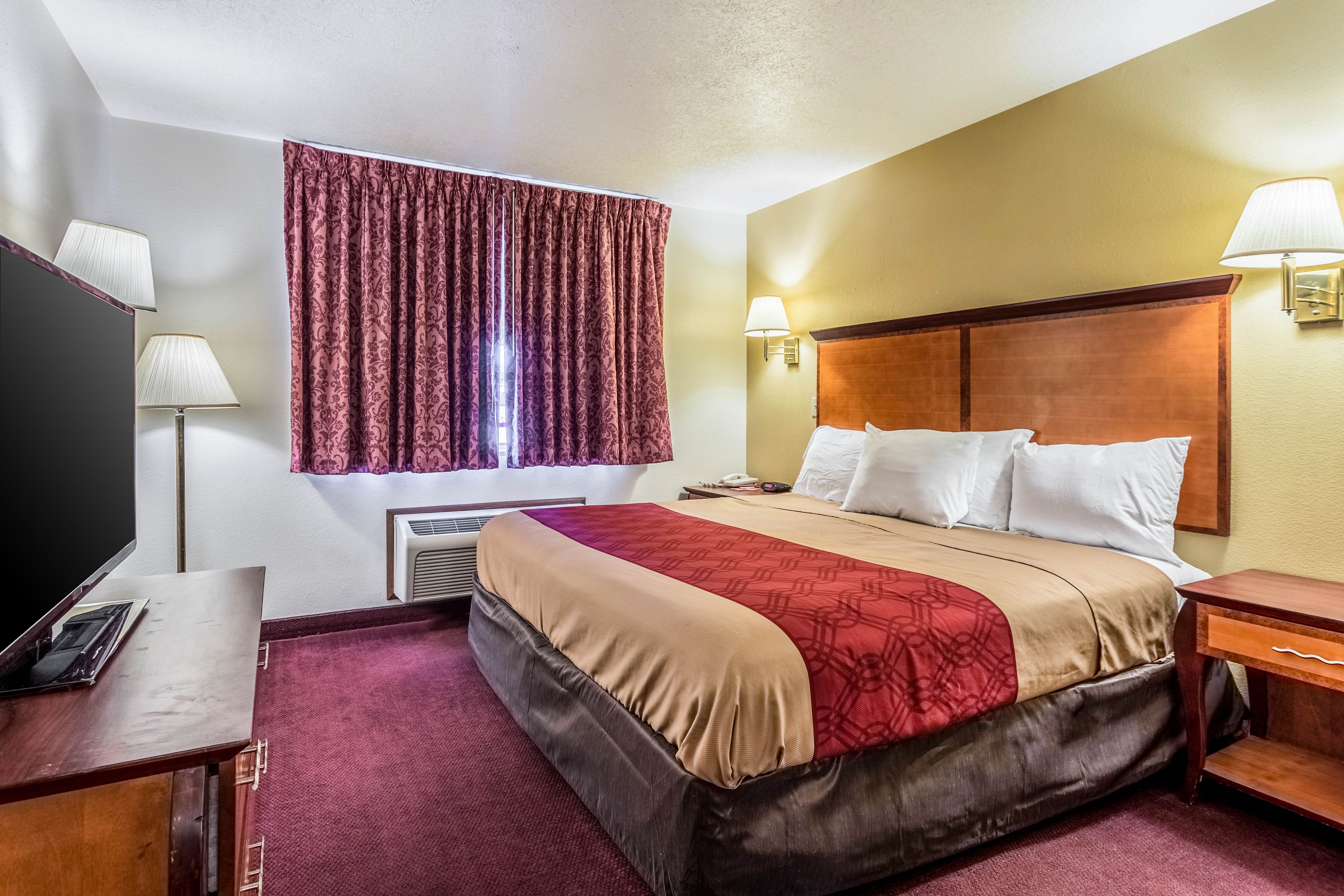 A hotel room with a large bed, bedside lamps, a desk with a telephone, and a window with curtains.
