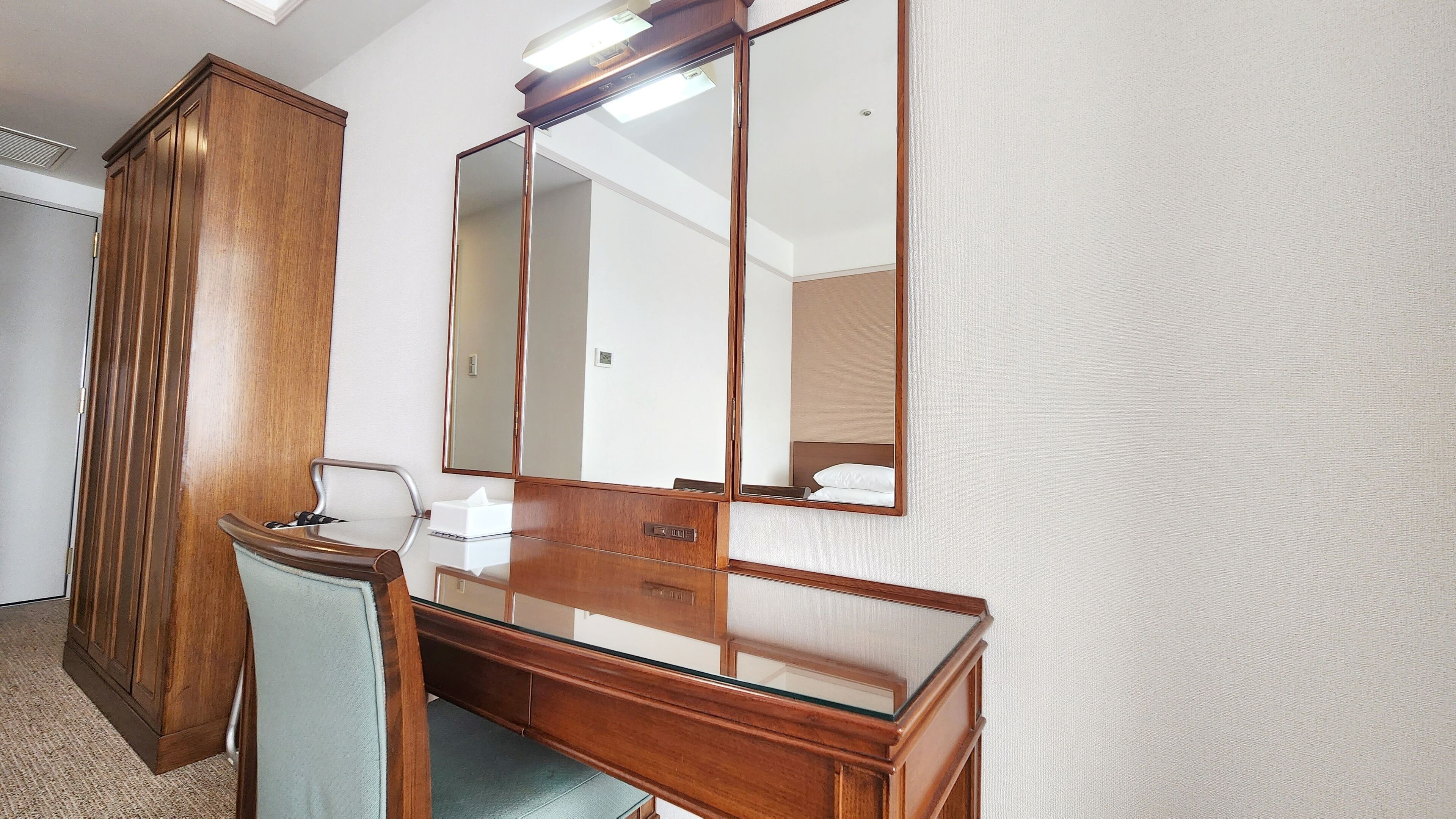 A hotel room with a wooden desk, a mirror, and a wardrobe.