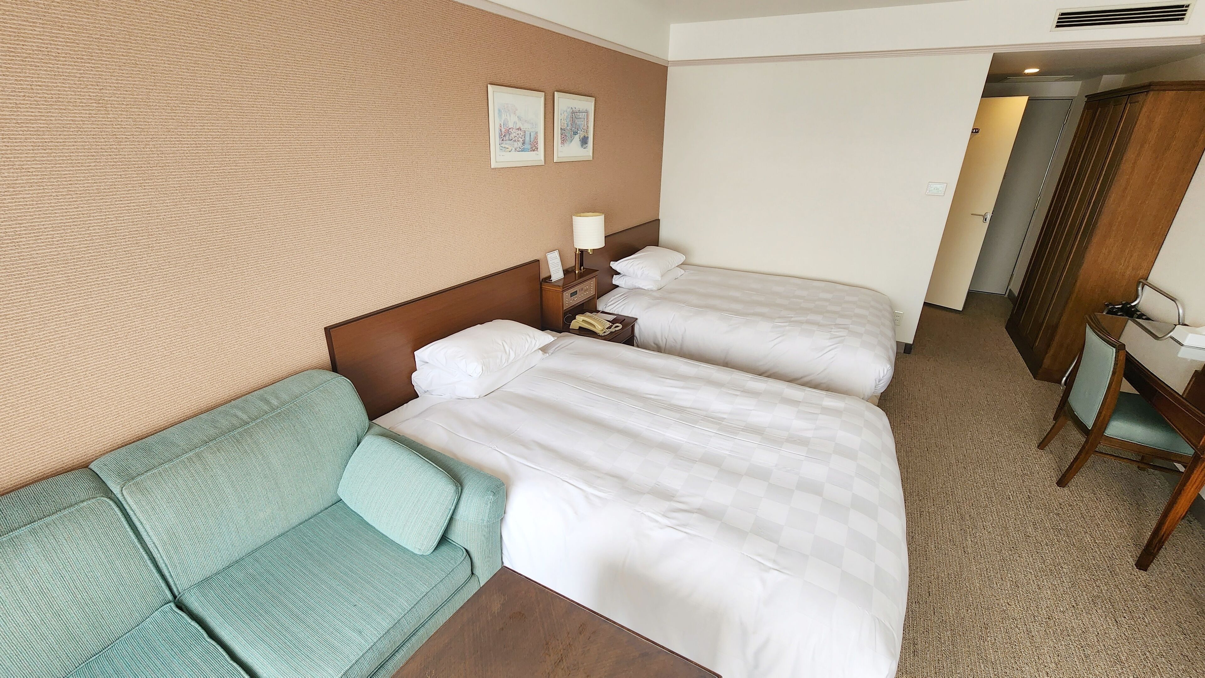 Ein Hotelzimmer mit zwei Betten, einem Schlafsofa, einem Schreibtisch und einem Stuhl.