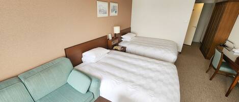 A hotel room with two beds, a sofa, a desk, and a chair.