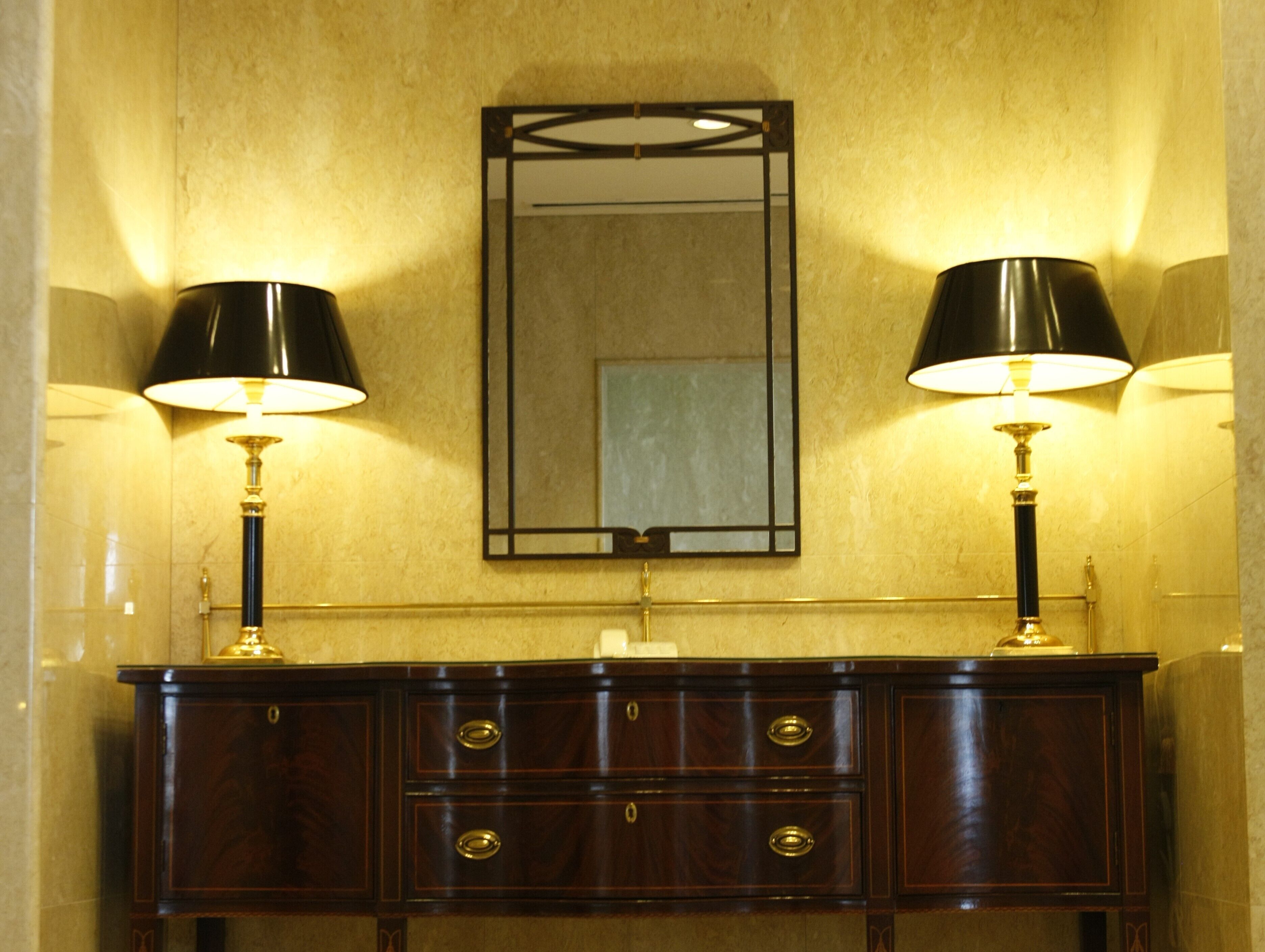 A bathroom with a wooden vanity, two wall-mounted lamps, and a mirror above the vanity.