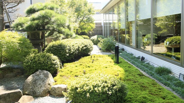 Un jardín japonés tradicional con formaciones rocosas, arbustos cuidadosamente podados y una pequeña estructura de madera.