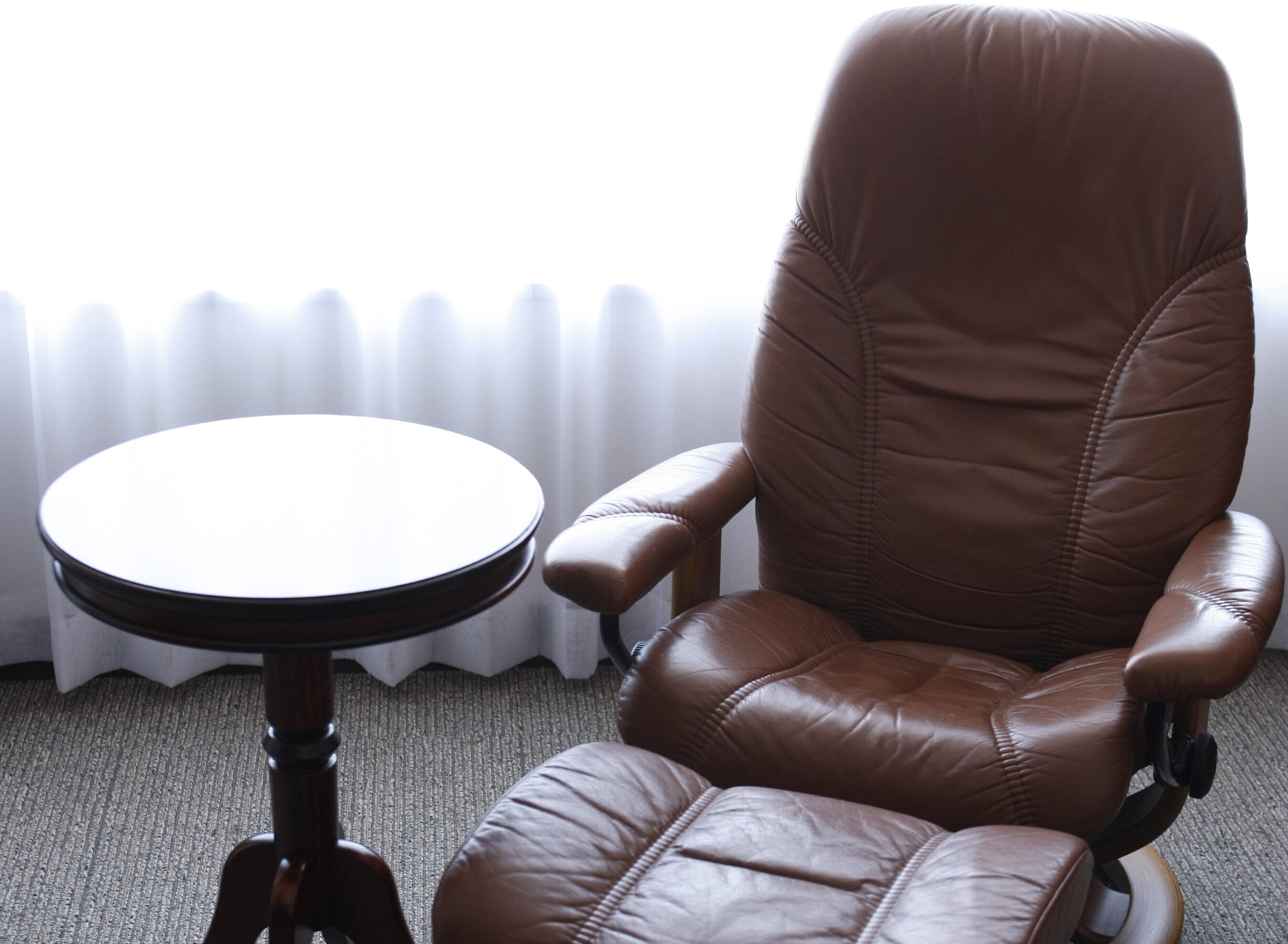 Un fauteuil en cuir marron avec un piétement en bois, et une table ronde placée à côté.