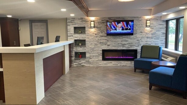 A reception area with a stone wall, a flat-screen TV, a fireplace, and seating. - Comfort Inn (Cornwall)