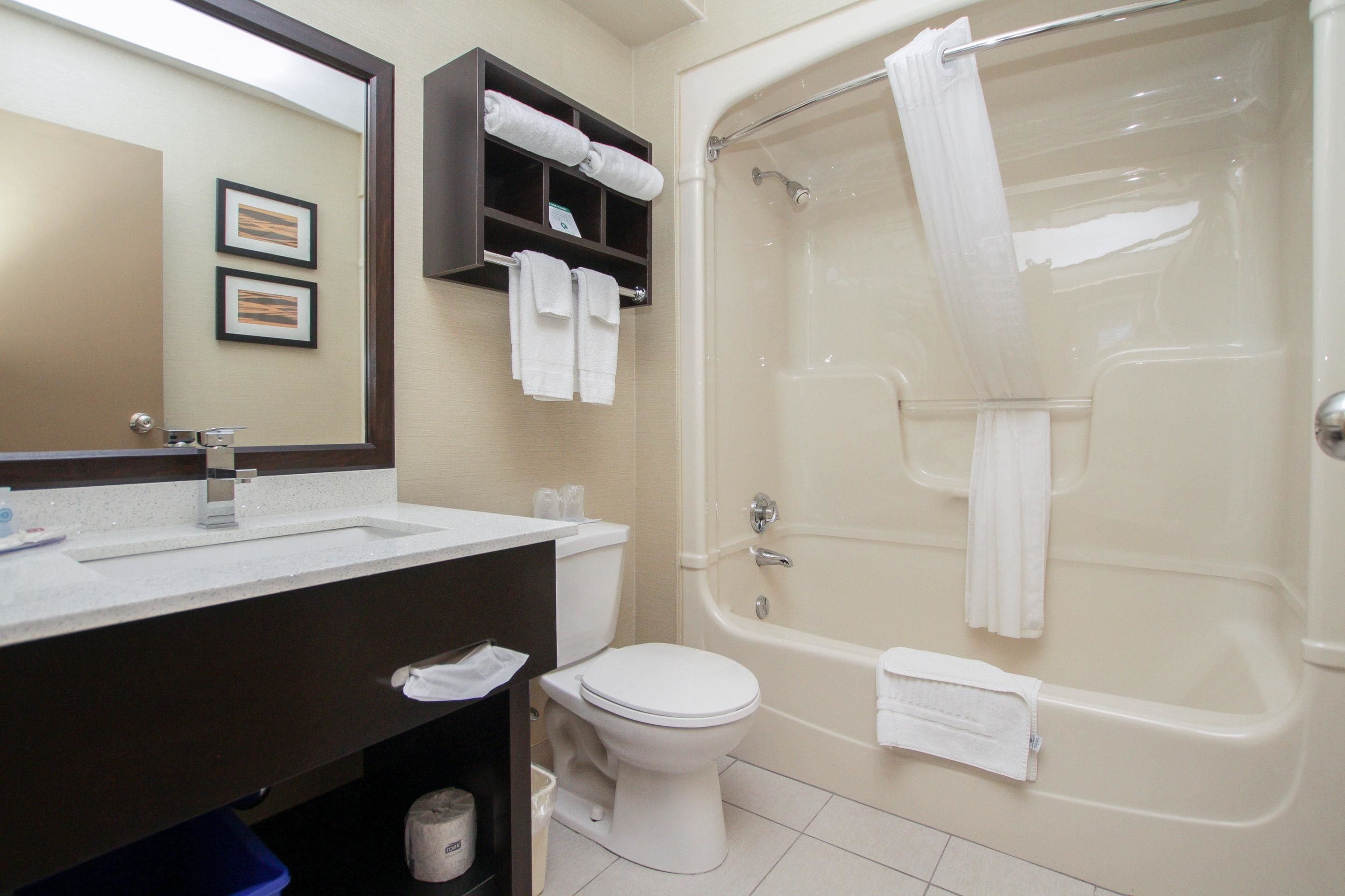 A bathroom with a sink, toilet, and bathtub. There are towels hanging on the wall and a shower curtain.