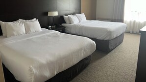 A hotel room with two beds, a nightstand with a lamp, and a large window with curtains. - Comfort Inn (Cornwall)