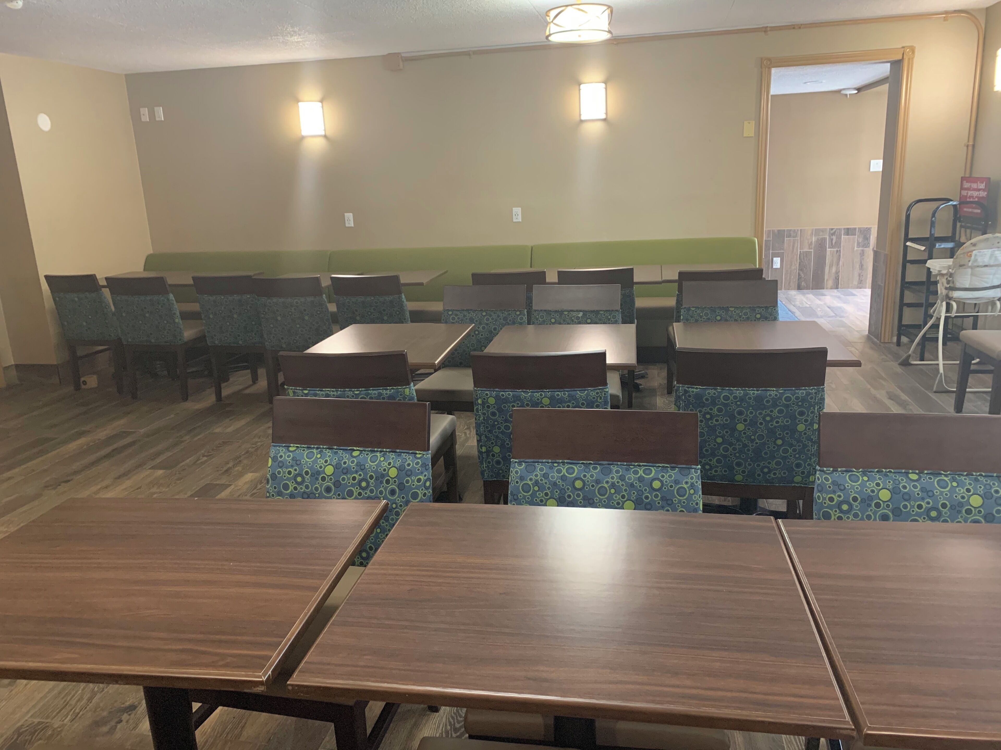 A dining area with multiple tables and chairs, a green accent wall, and a visible door leading to another room.