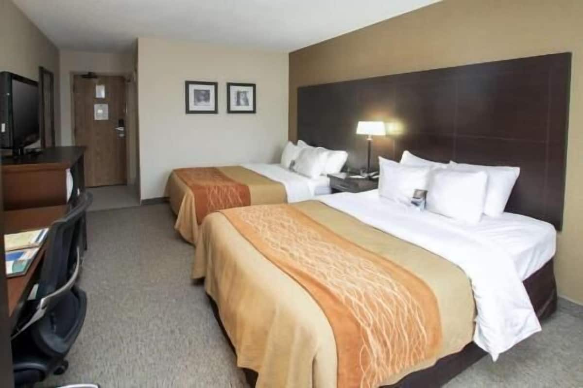 A hotel room with two beds, a desk, a chair, and a television.