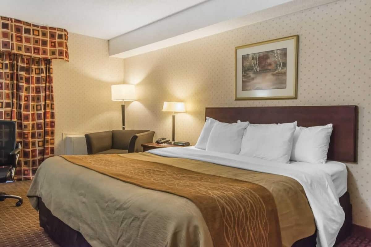 A hotel room with a large bed, two bedside lamps, a chair, a desk, and a painting on the wall.
