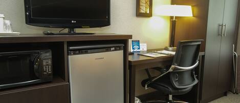 Habitación de hotel con televisión de pantalla plana, microondas, refrigerador pequeño, escritorio con silla, lámpara y armario.