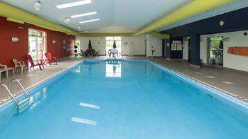Une piscine intérieure avec des couloirs clairement délimités, un poste de surveillance pour le sauveteur et un espace détente avec des tables et des chaises.