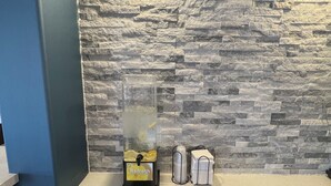 A counter with a stone wall backdrop, a beverage dispenser, and a trash bin. - Comfort Inn (Cornwall)