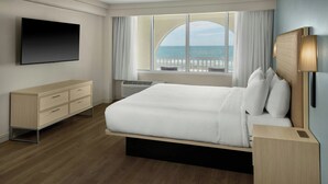 Ein modernes Hotelzimmer mit einem großen Bett, einem Flachbildfernseher, einer hölzernen Kommode und Meerblick.