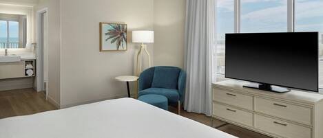 Habitación de hotel con cama, televisor en una cómoda, una silla, una mesita y ventana con cortinas.