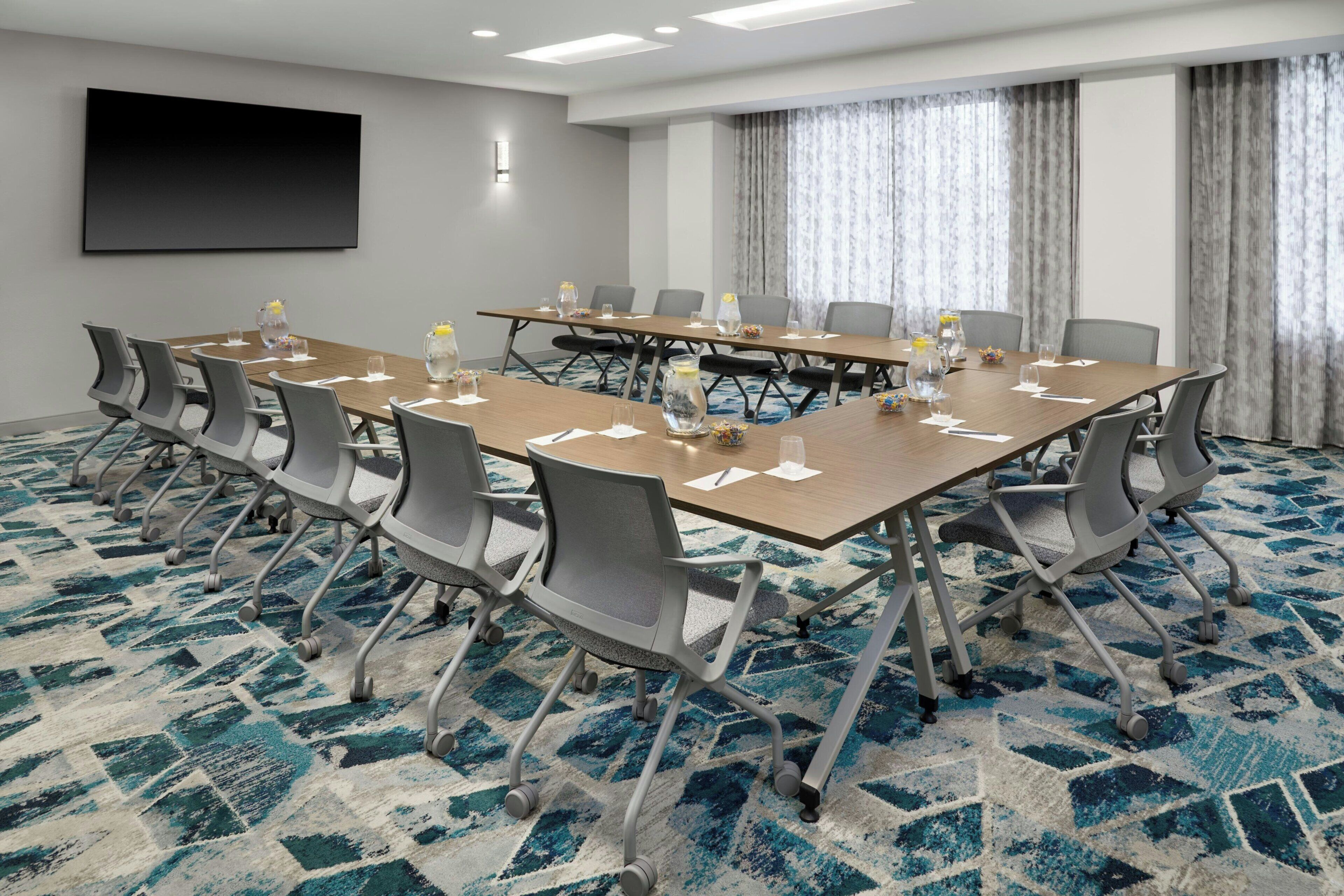 A conference room with a large table, chairs, a TV screen, and a patterned carpet.