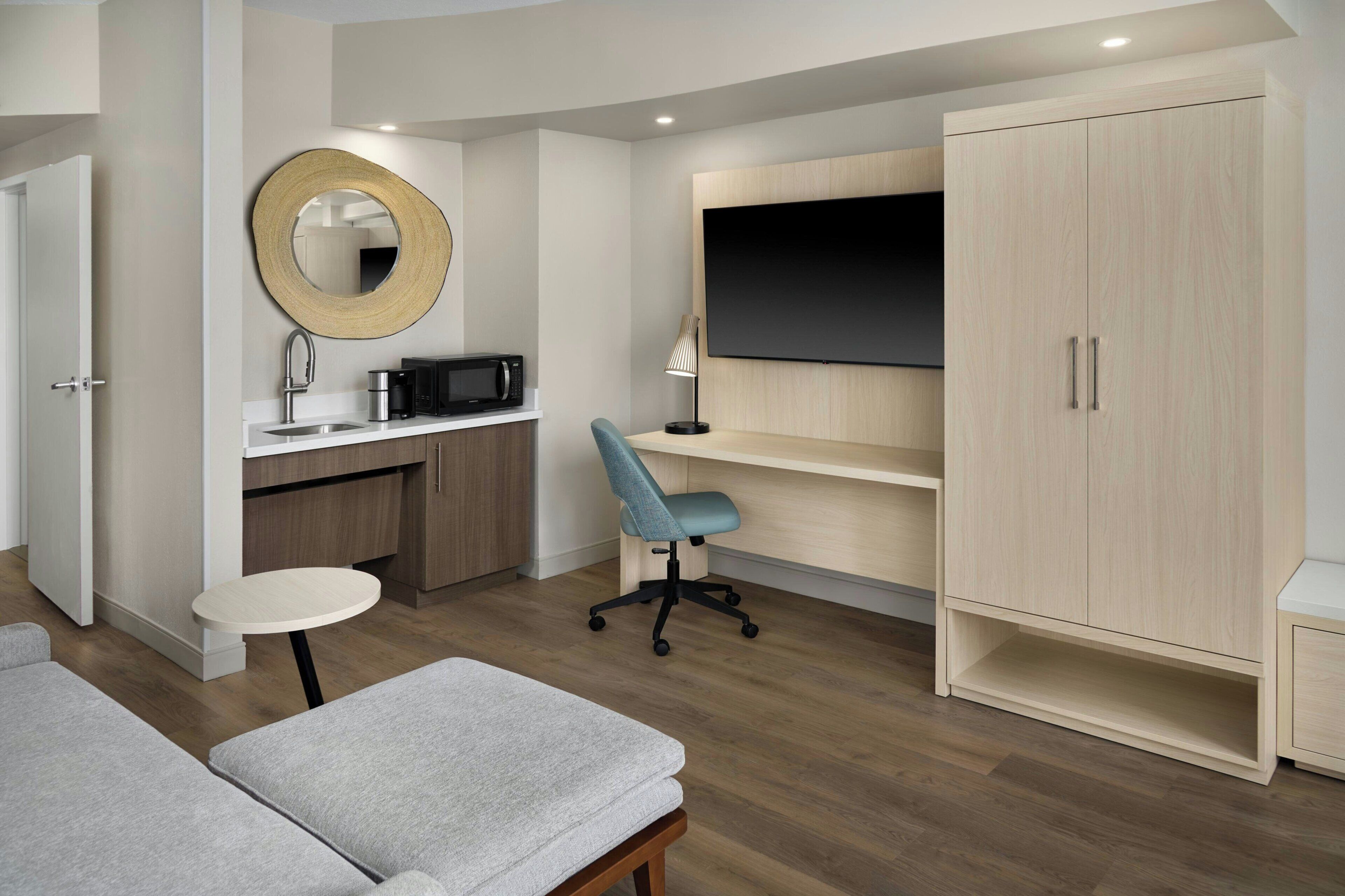 Een moderne kamer met een kitchenette, een flatscreen-tv, een bureau met stoel en een kledingkast.