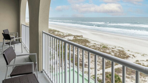 A balcony with a view of the beach, a wooden walkway, and a chair.