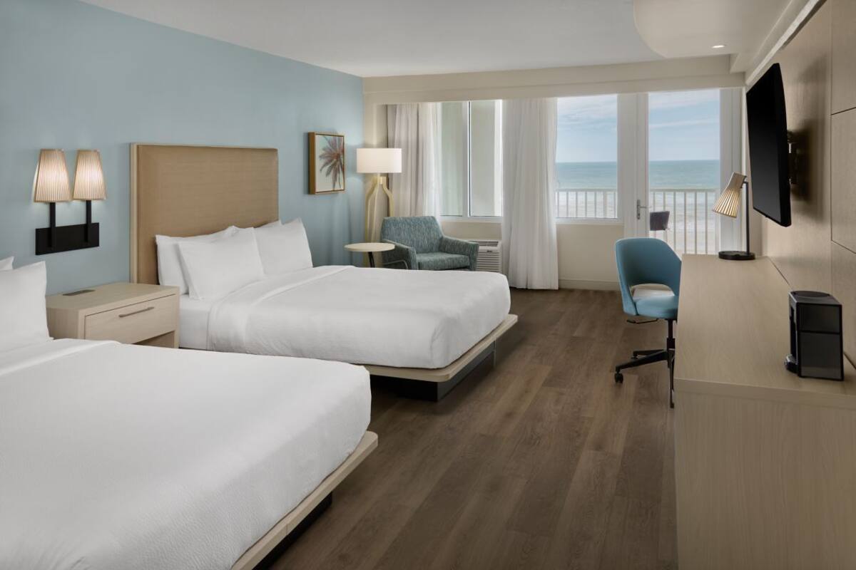 Habitación de hotel con dos camas, un escritorio, una silla, televisión y vista al océano.