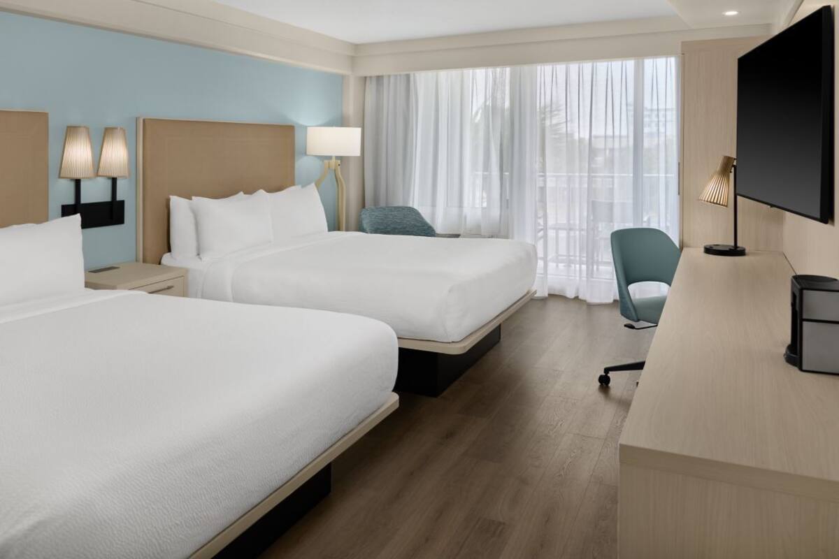 Habitación de hotel con dos camas, un escritorio, una silla y un televisor.