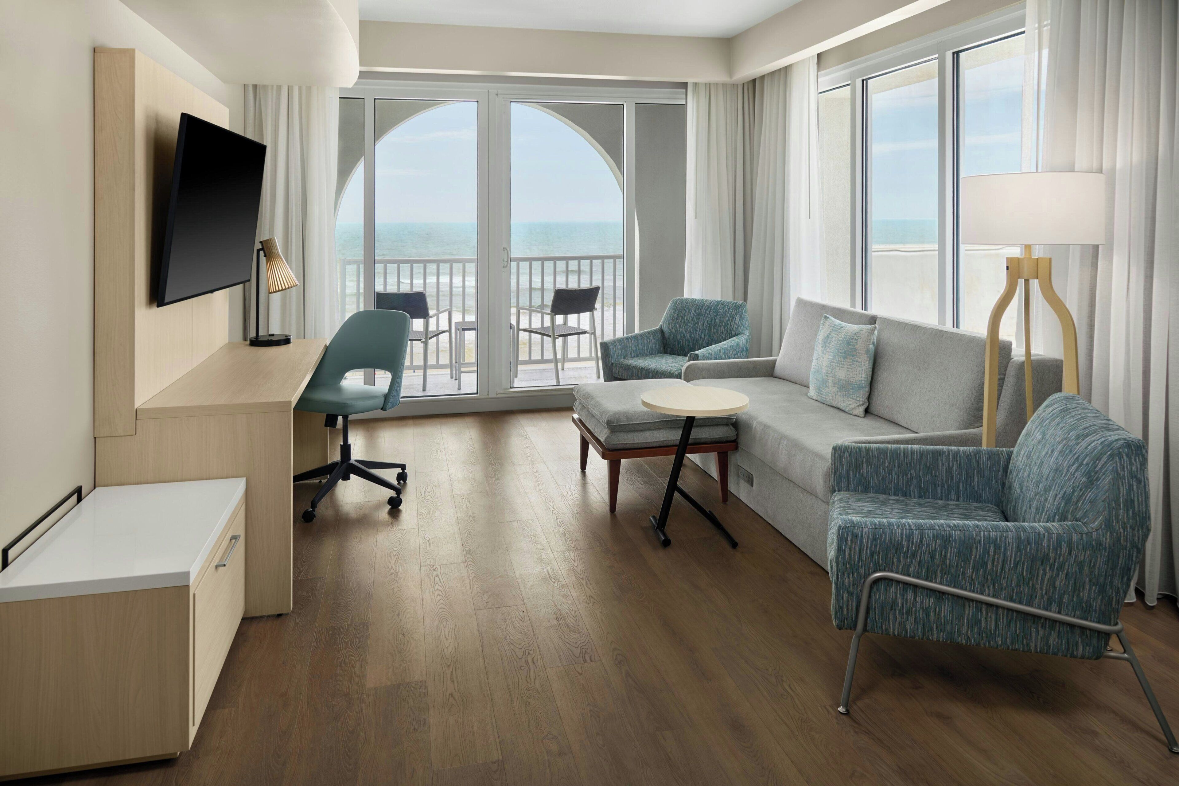Une chambre d’hôtel équipée d’une télévision à écran plat, d’un bureau, d’un canapé, d’une chaise et d’un balcon avec vue sur l’océan.