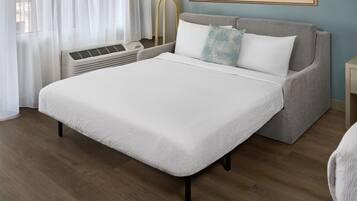 A neatly arranged bedroom with a bed, a sofa, a lamp, and a wall-mounted air conditioner.