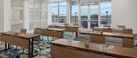 A conference room with multiple tables, chairs, and large windows with blinds.