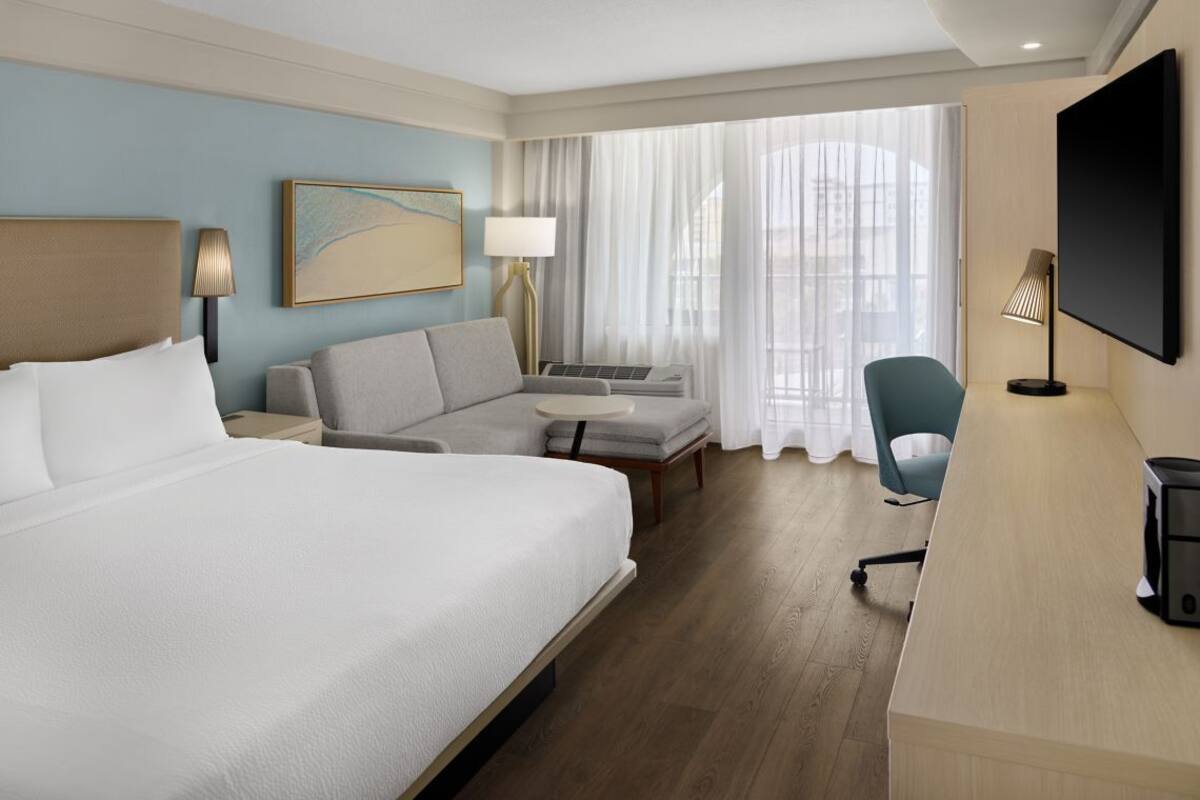 Habitación de hotel con una cama grande, un sofá, un escritorio, un televisor y una ventana con cortinas.