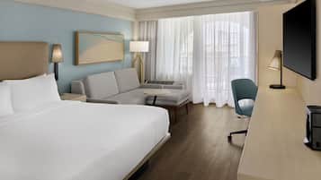 A hotel room with a large bed, a sofa, a desk, a TV, and a window with curtains.