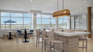 A modern dining area with a large island, multiple seating options, and large windows offering a view of the beach.