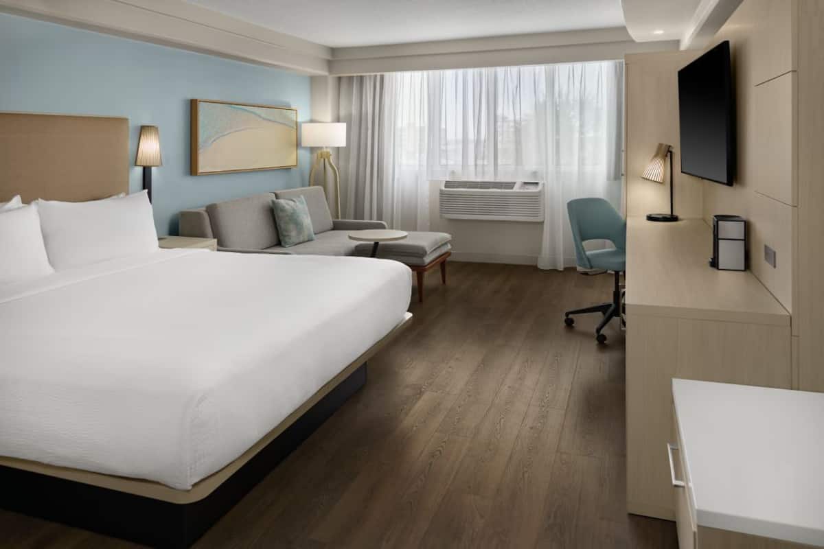 Habitación de hotel con una cama grande, un escritorio, una silla, un televisor y una ventana con cortinas.