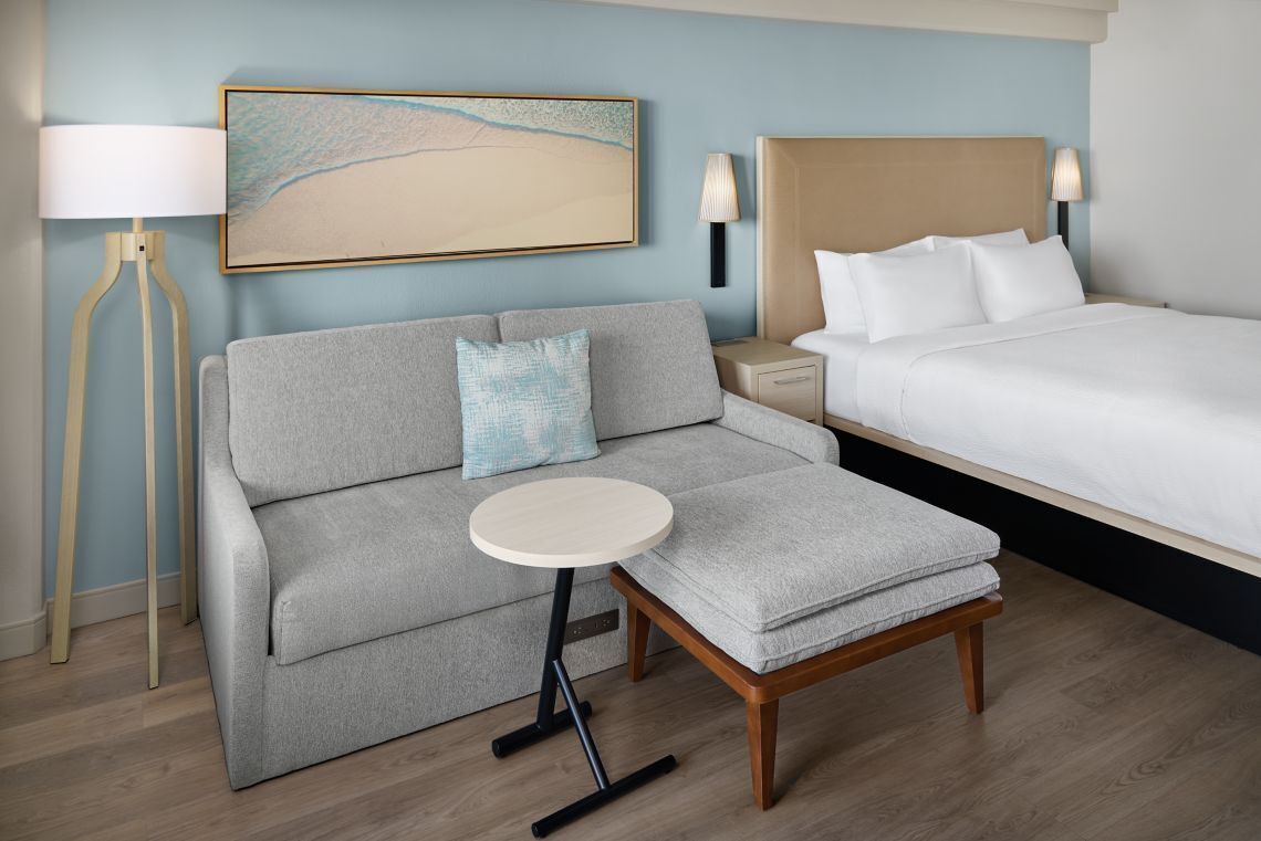 Una habitació d'hotel amb llit, sofà, taula petita i làmpada.