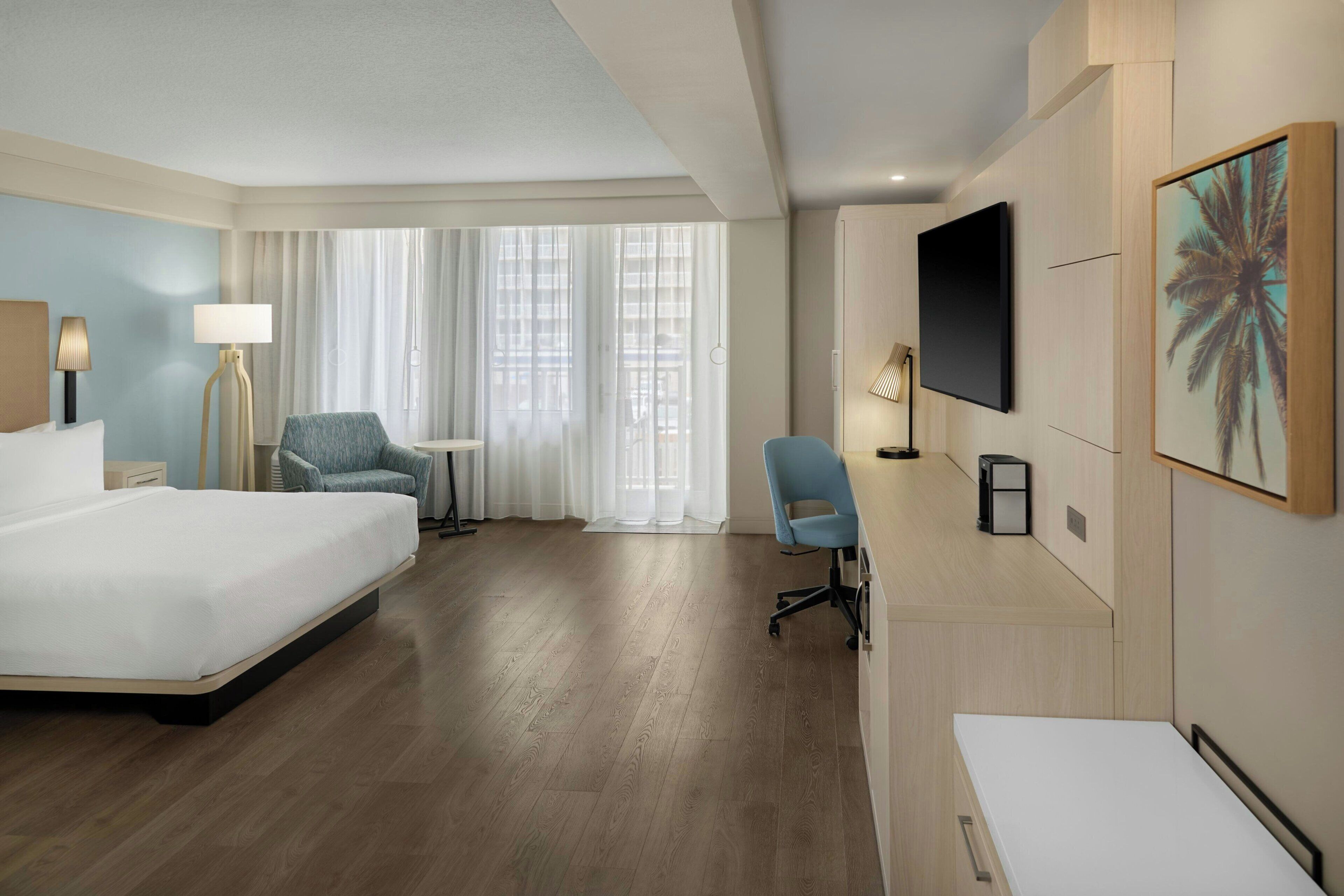 A hotel room with a large bed, a desk, a chair, a TV, and a window with curtains.