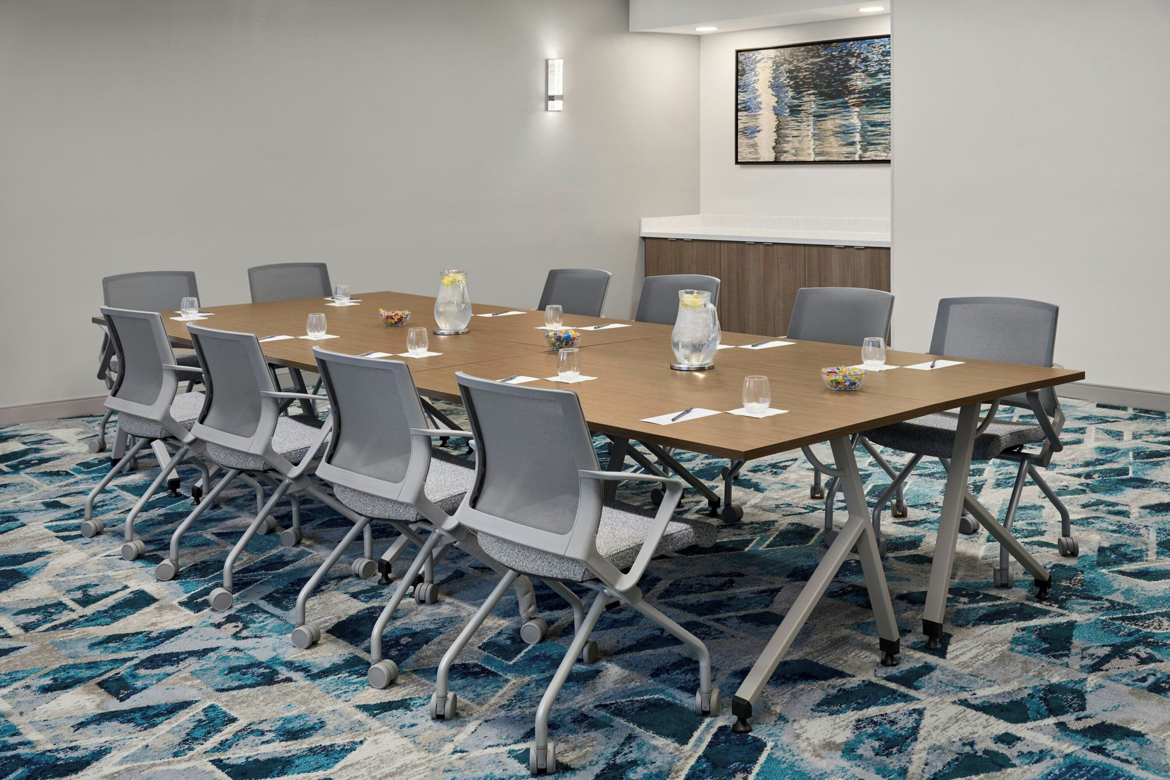A conference room with a long table, gray chairs, and a patterned carpet.