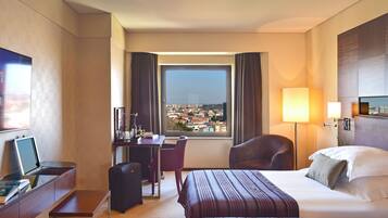 Habitación de hotel con cama, escritorio, silla y vistas a la ciudad a través de un ventanal grande.