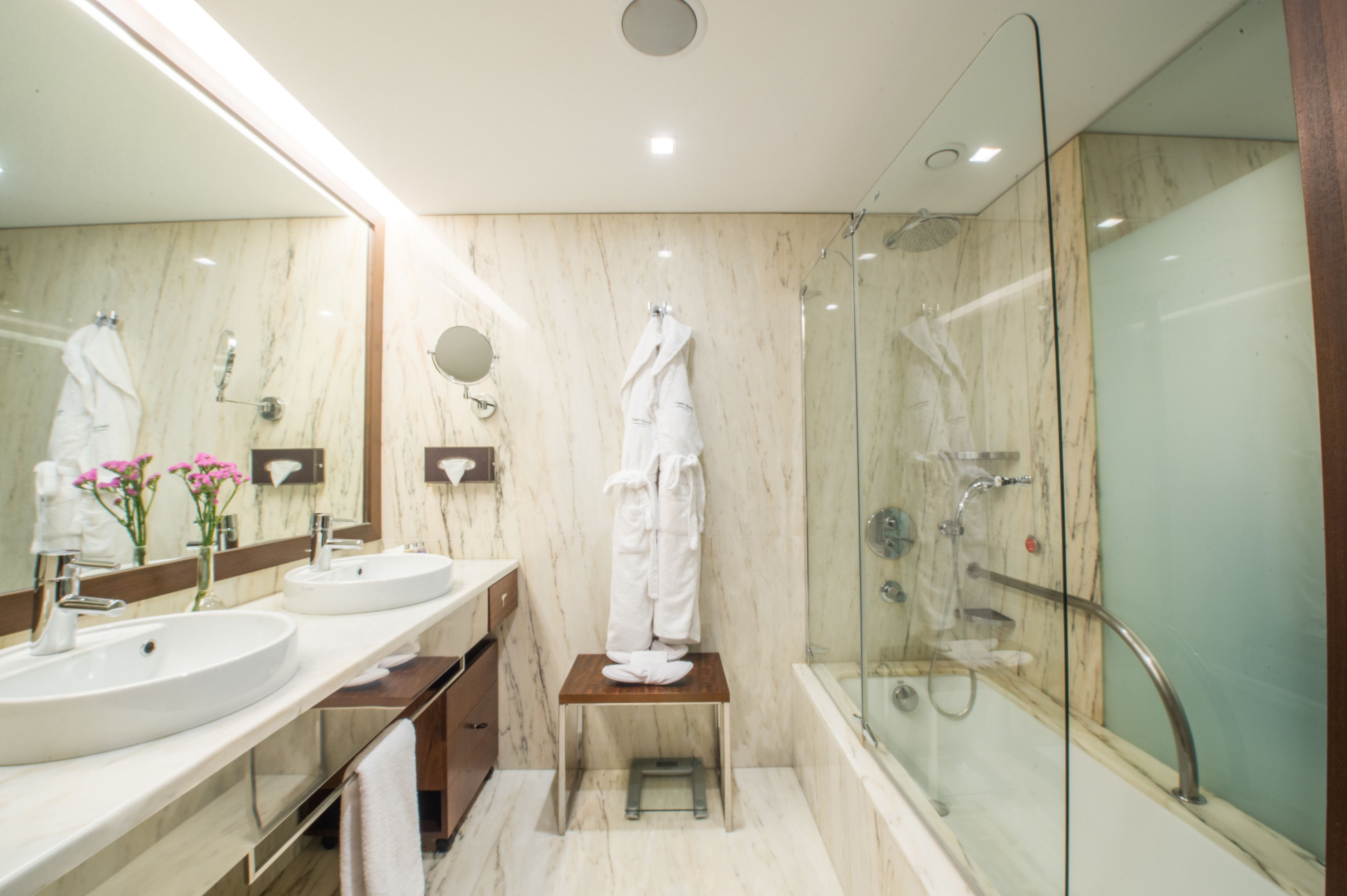 Un baño moderno con dos lavamanos, un espejo grande, cabina de ducha de vidrio y un taburete de madera.