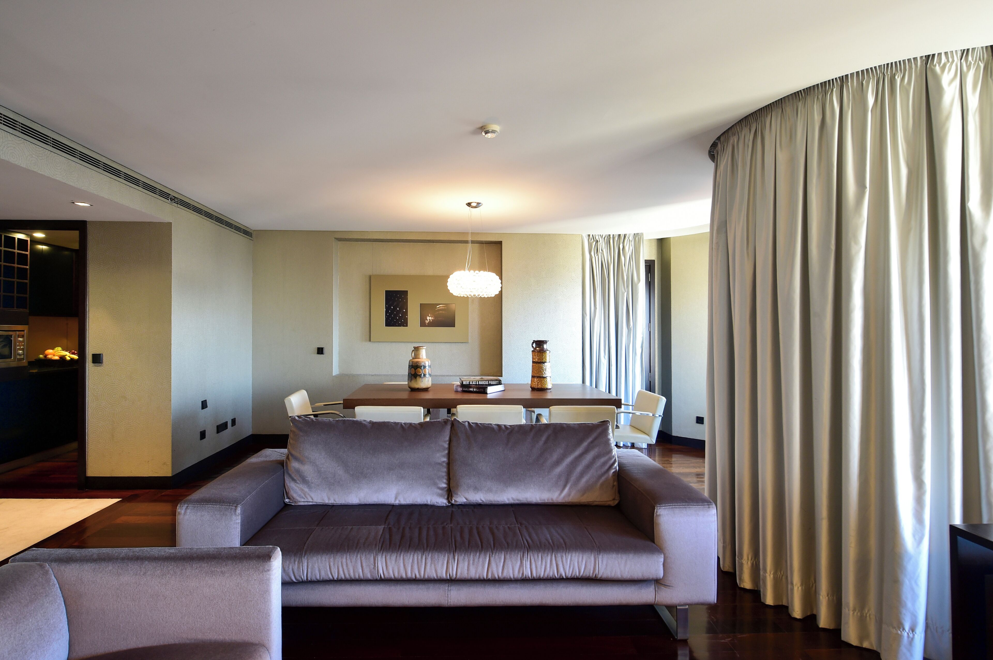 Una sala de estar moderna con un sofá, una mesa de comedor y un ventanal con cortinas.