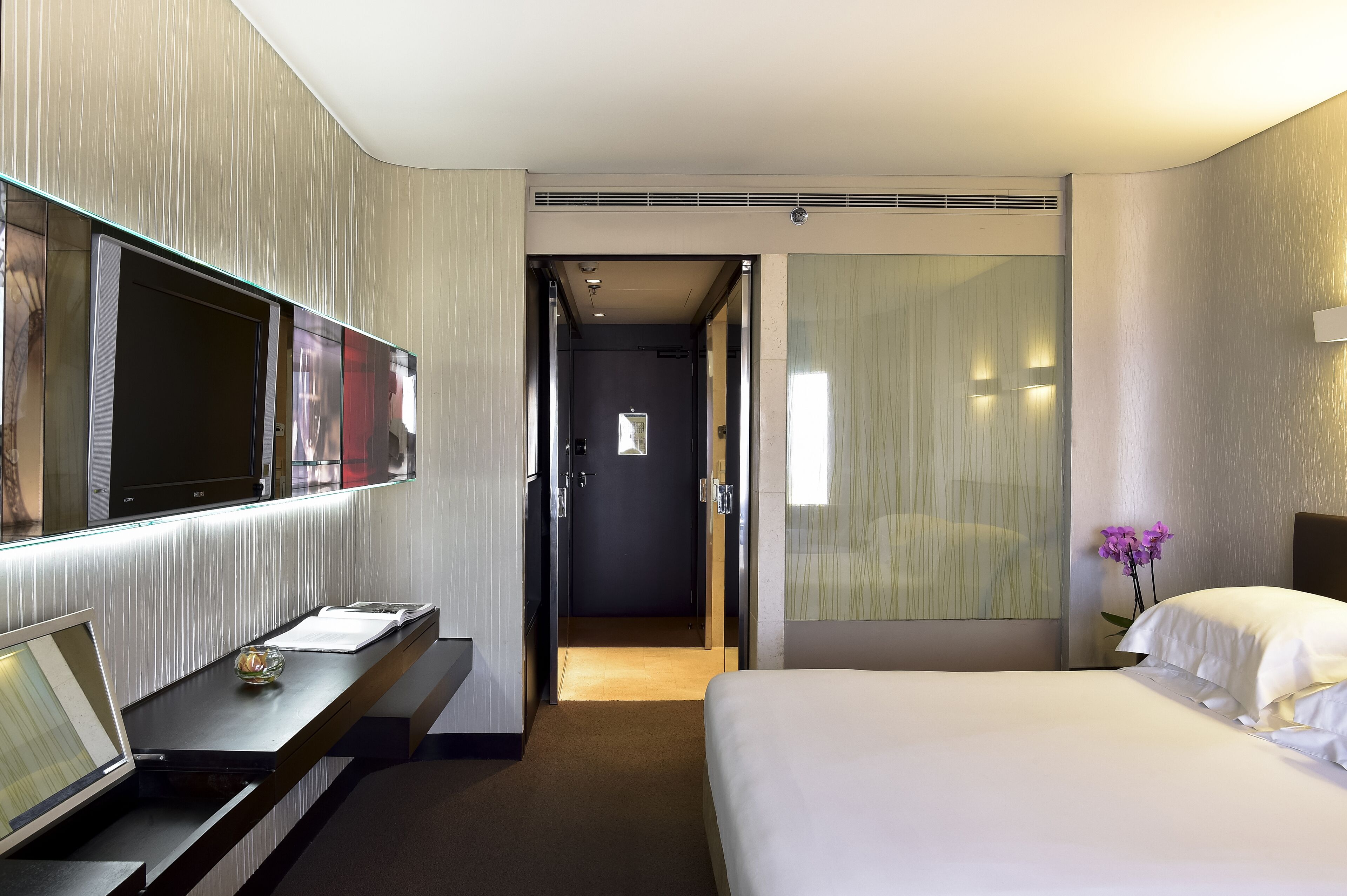 Une chambre d’hôtel avec un lit, un bureau avec un ordinateur portable, une télévision et une porte donnant sur une autre pièce.