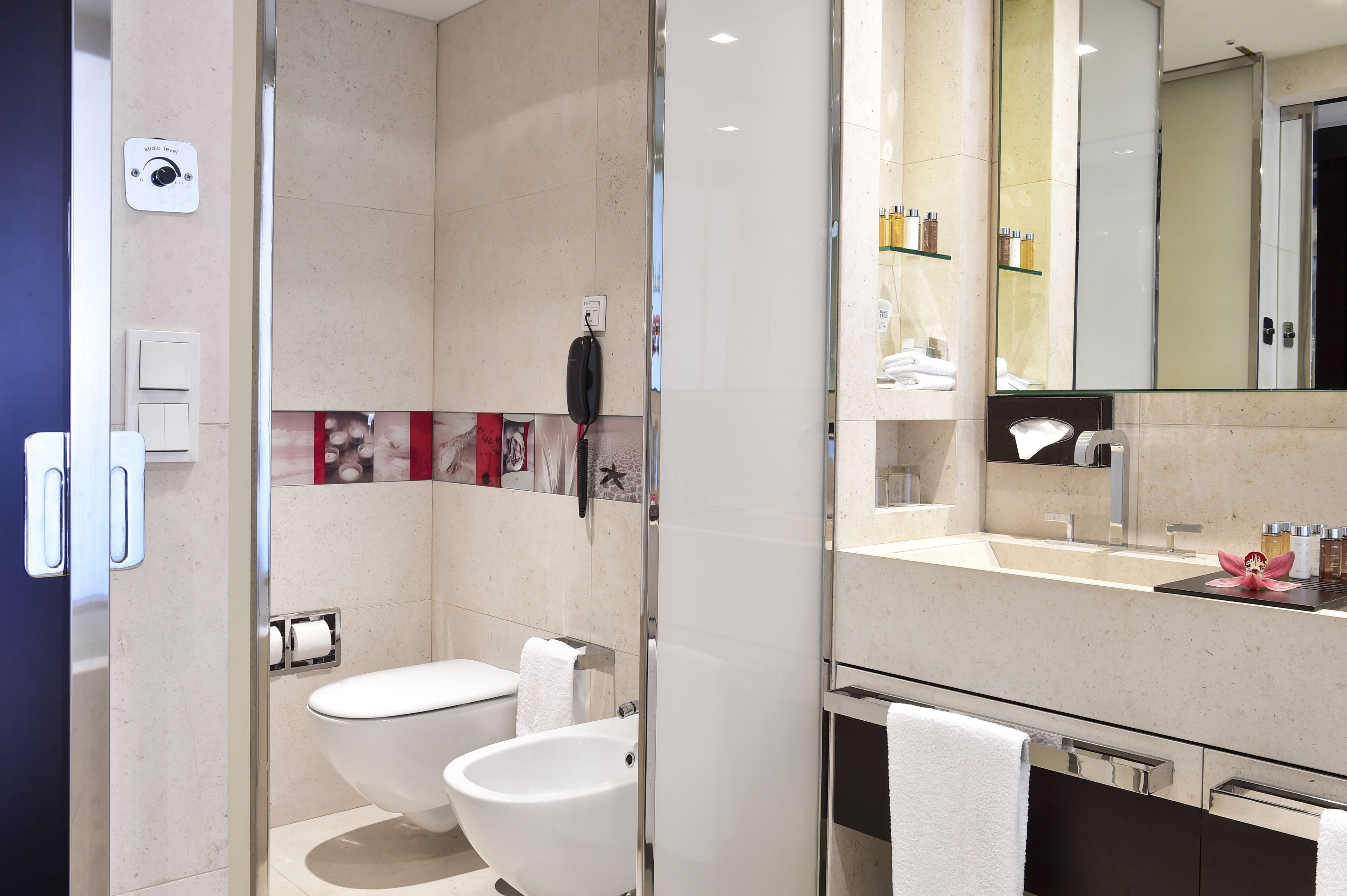 Et moderne badeværelse med glasbrusekabine, toilet, bidet og et vaskebord med spejl.