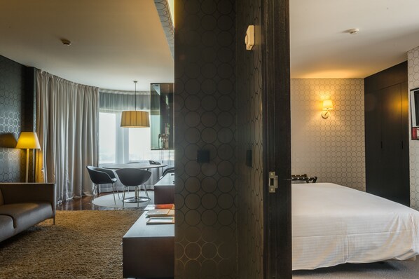 A modern hotel room with a large bed, a desk with a chair, a sofa, and a dining area with a table and chairs. - Porto Palácio Hotel by The Editory (Porto)
