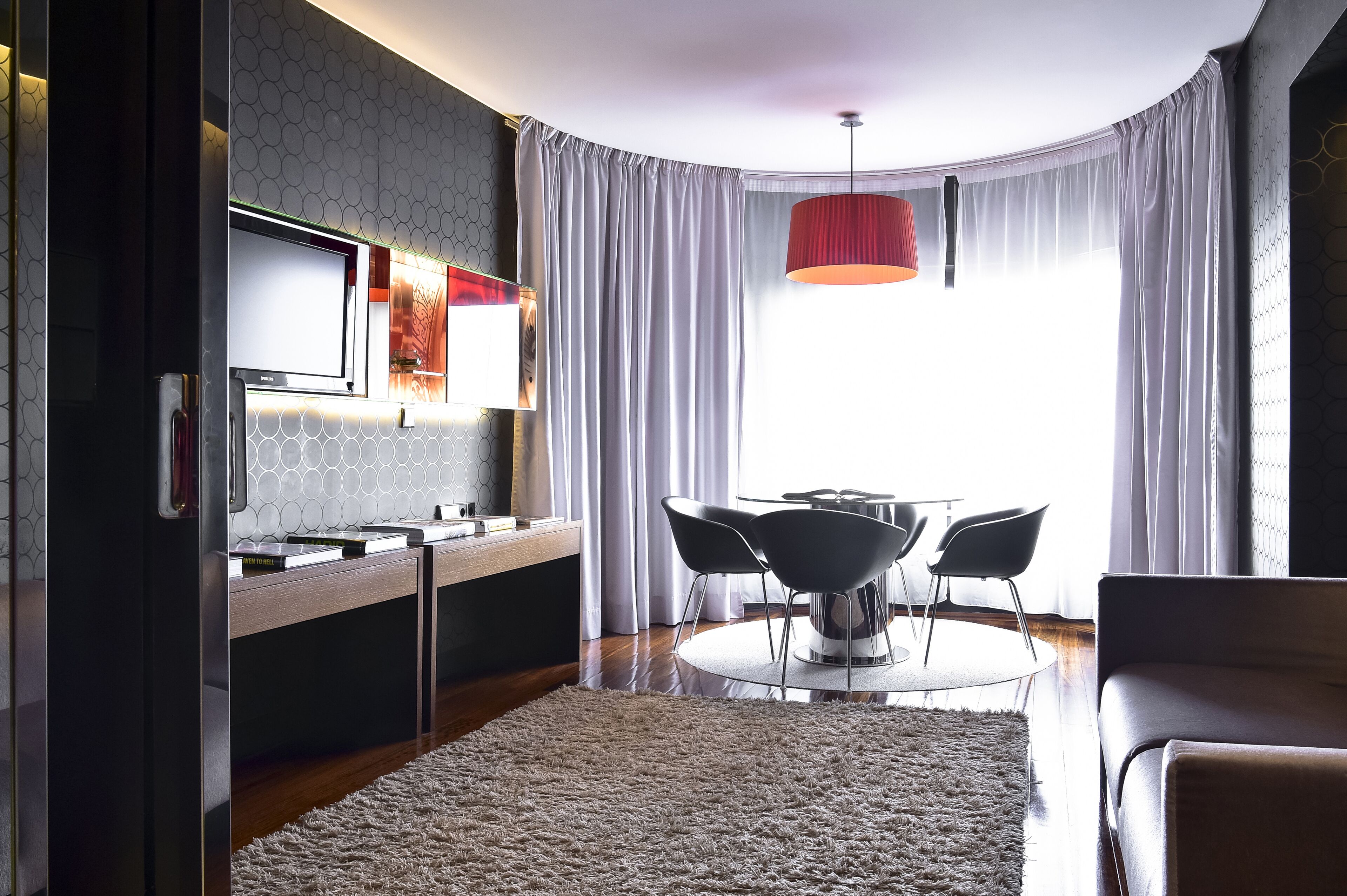 A modern kitchen with a built-in oven, a dining area with a round table and four chairs, and a large window with curtains.