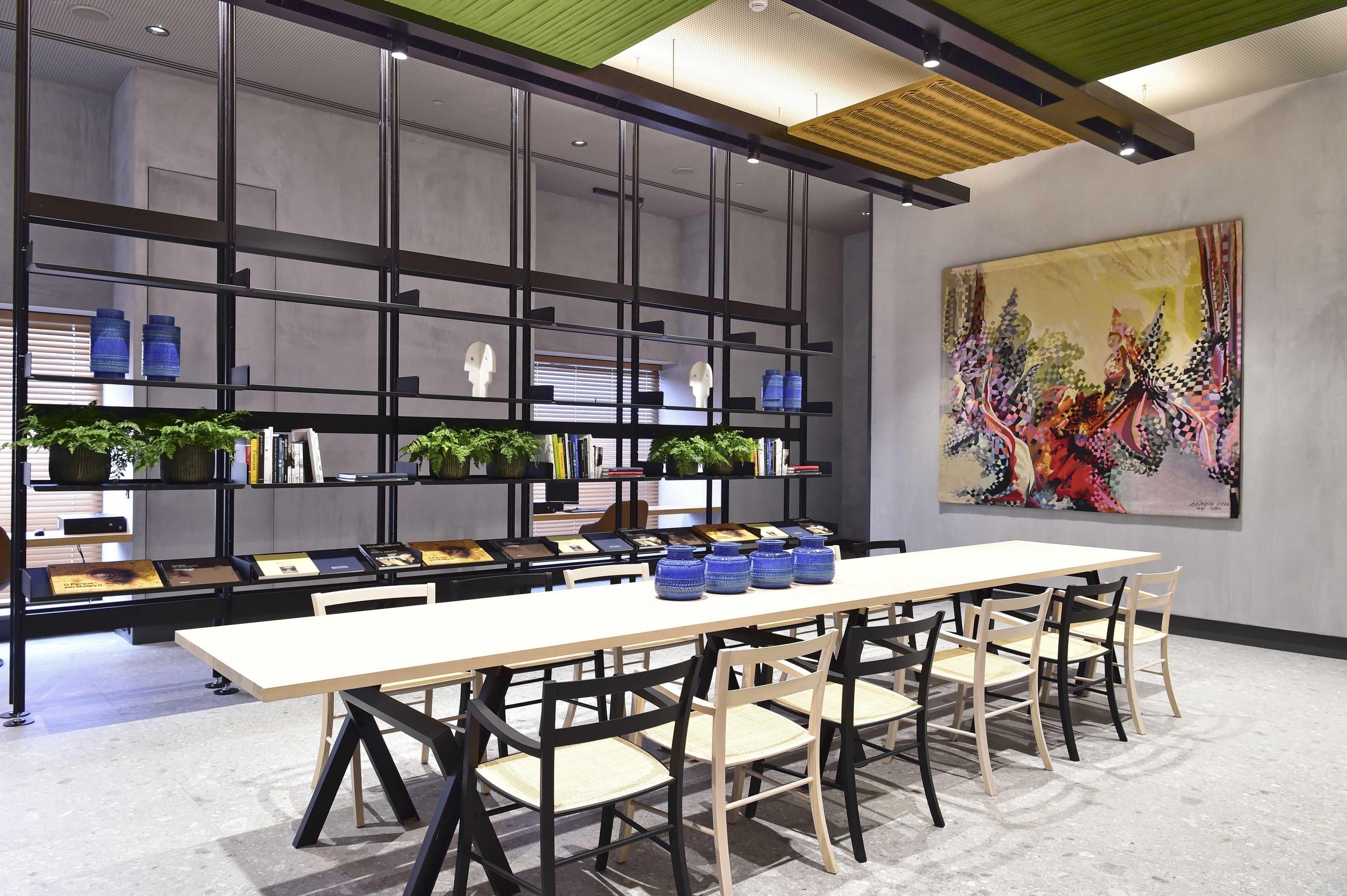 A modern conference room with a long table, chairs, and a bookshelf with plants and books.