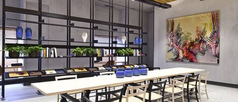 A modern conference room with a long table, chairs, and a bookshelf with plants and books.