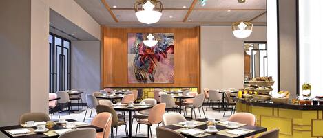 A modern hotel dining area with multiple tables and chairs, a central counter with food and beverages, and a large abstract painting on the wall.