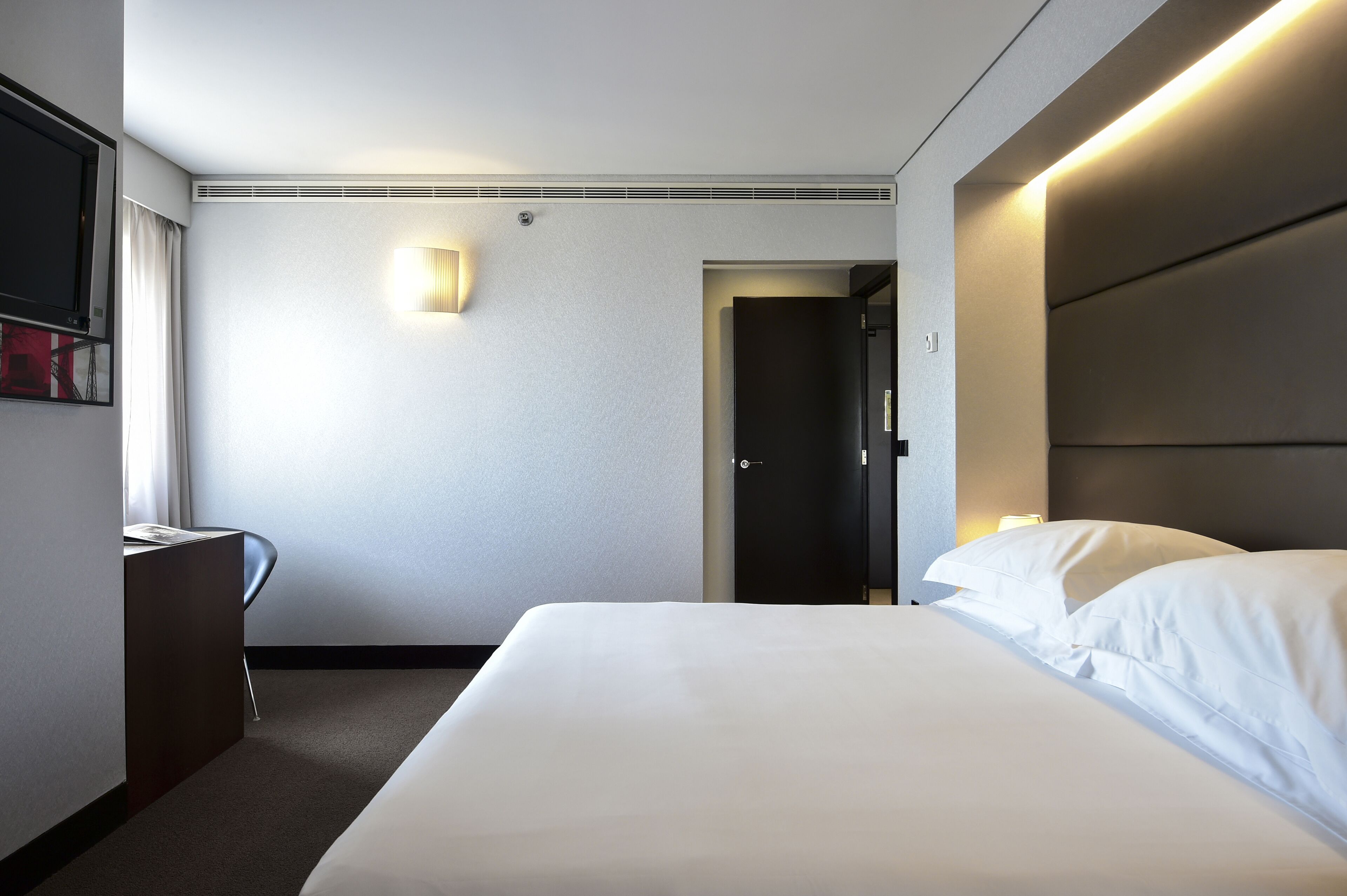 A hotel room with a large bed, a desk, a chair, a flat-screen TV, and a door.